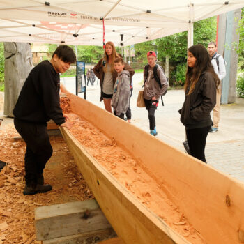 Apprentice Carver Brandon Hall of Squamish Nation talking to guests about carving the Community Reconciliation Canoe.