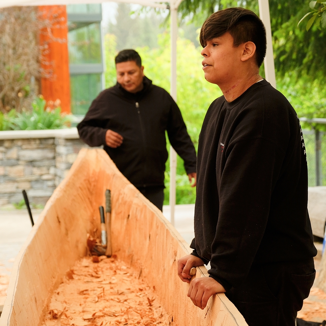 Master Carver Ray Natraoro and Apprentice Brandon Hall working on the Community Reconciliation Canoe