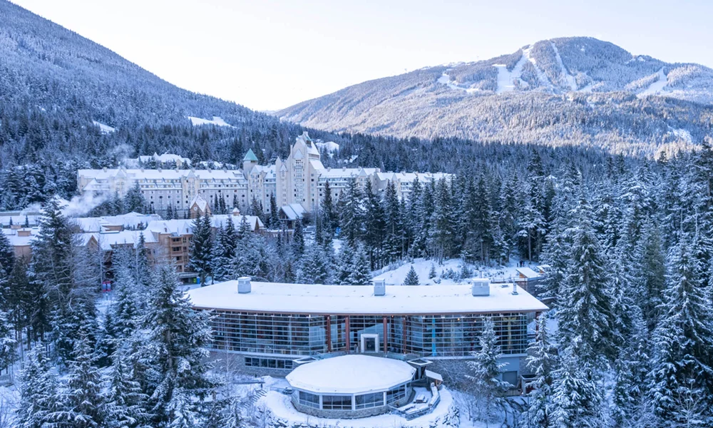 Winter aerial view of the Squamish Lil'wat Cultural Centre covered in snow, surrounded by Whistler's breathtaking mountain landscapes.